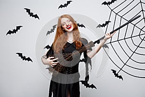 Halloween Concept - Happy elegant witch enjoy playing with broomstick halloween party over grey background.