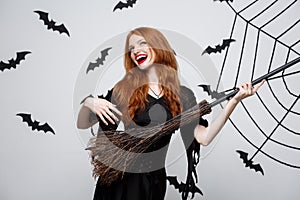 Halloween Concept - Happy elegant witch enjoy playing with broomstick halloween party over grey background.