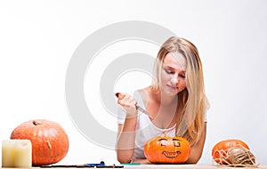 Halloween concept, happy Girl sitting at table with pumpkins preparing for holiday with candle and rope, cut Jack lantern, funny