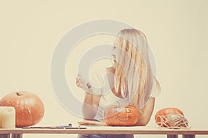 Halloween concept, happy Girl sitting at table with pumpkins preparing for holiday with candle and rope, cut Jack lantern, funny
