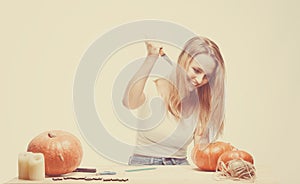 Halloween concept, happy Girl sitting at table with pumpkins preparing for holiday with candle and rope, cut Jack lantern, funny