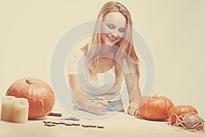 Halloween concept, happy Girl sitting at table with pumpkins preparing for holiday with candle and rope, drawing how to do Jack