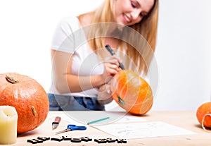 Halloween concept, happy Girl sitting at table with pumpkins preparing for holiday with candle and rope, drawing how to do Jack l