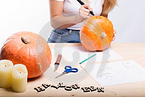 Halloween concept, happy Girl sitting at table with pumpkins preparing for holiday with candle and rope, drawing how to do Jack l