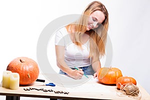 Halloween concept, happy Girl sitting at table with pumpkins preparing for holiday with candle and rope, drawing how to do Jack l