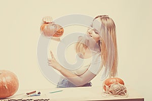 Halloween concept, happy Girl sitting at table with pumpkins preparing for holiday with candle and rope, holding Jack lantern,