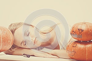 Halloween concept, happy Girl sitting at table with pumpkins preparing for holiday with candle and rope, sleeping on table near