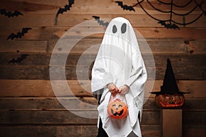 Halloween Concept - little white ghost with halloween pumpkin candy jar doing trick or treat with curved pumpkins over bats and sp