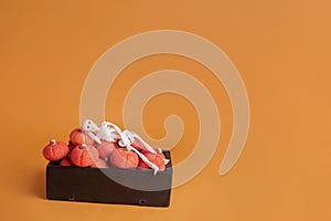 Halloween concept, skeleton sleeping on wooden box with marshmallow pumpkins on orange background