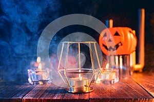 Halloween concept, spooky decorations with lighting up candle and candle holder with blue tone smoke around on a dark wooden table