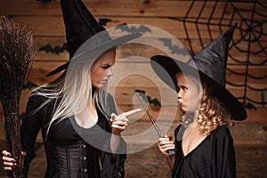 Halloween Concept - stressful witch mother teaching her daughter in witch costumes celebrating Halloween over bats and spider web