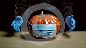 Halloween and coronavirus concept. close-up of woman putting pumpkin in mask on table.