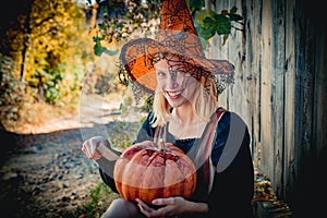 Halloween costume. Happy young woman in witch halloween costume on party cutting pumpkin. Emotional young woman in