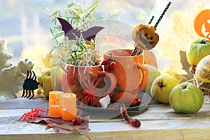 Halloween decor, a couple of cups with a drink, decorative candles, pumpkins, berries, leaves on the windowsill