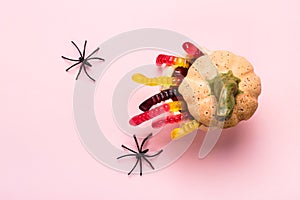 Halloween decorations. Pumpkin with treat of marmalade worms and spiders on pink background