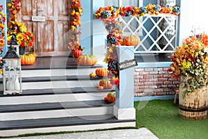 Halloween design home with yellow fall leaves. House entrance staircase decorated for autumn holidays, fall flowers and pumpkins.