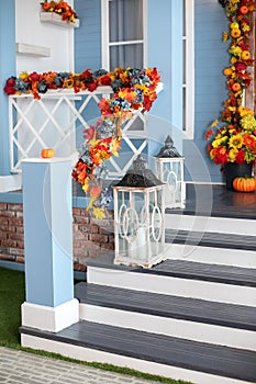 Halloween design home with yellow fall leaves and lamps. House entrance staircase decorated fall flowers and pumpkins.