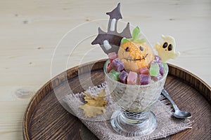 Halloween dessert in a glass. It consists of ice cream in the form of a ghost pumpkin, a white chocolate ghost and a black chocol