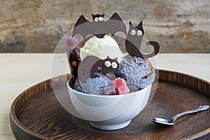 Halloween dessert in a white cup. It consists of ice cream and chocolate black cats, bat.