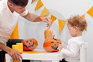 Halloween family activity, pumpkin painting process. Cute child drawing scary face. Holiday preparation, party decor