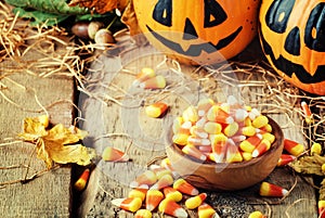 Halloween festive composition with sweet corn in bowl and smiling pumpkins guards, lantern, straw and fallen leaves on dark