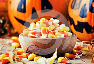 Halloween festive composition with sweet corn in bowl and smiling pumpkins guards, lantern, straw and fallen leaves on dark