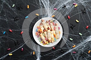 Halloween finger cookies with candies and spider webs on black background. Halloween food concept