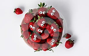 Halloween food. Funny strawberry face with eyes in a white plate on a white background. Creepy food. Halloween background. View