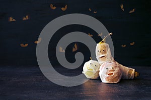 Halloween Fruit Mummy. Funny Scared orange, apple and banana with eyes and wrapped in bandages on dark background. Halloween DIY c