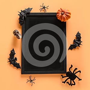 Halloween fun party decorations, pumpkins, candy bowl, bat, skulls, spooky spider on orange. Overhead view. Copy space