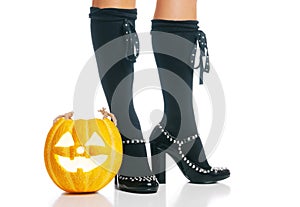 Halloween glowing pumpkin near female legs in black shoes.