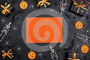 Halloween holiday background with blank orange card surrounded by gifts and decorations on black backdrop