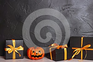 Halloween holiday background with gifts and pumpkin head Jack lantern with funny faces against a black wall