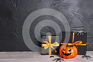 Halloween holiday background with gifts and pumpkin head Jack lantern with funny faces against a black wall