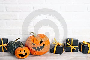 Halloween holiday background with gifts and pumpkin head Jack lantern with funny faces against a white brick wall