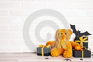 Halloween holiday background with orange toy bear, gifts and decorations against a white brick wall