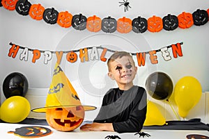 Halloween holiday concept. Cute boy in costume sitting behind a table in Halloween theme decorated room