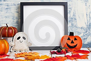 Halloween holiday concept with empty black frame and pumpkins on a light table against a light wall. copy space