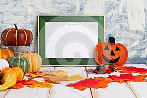 Halloween holiday concept with empty green frame and pumpkins on a light table against a light wall. copy space