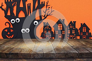 Halloween holiday concept. Empty rustic table in front of haunted village over orange background. Ready for product display montag