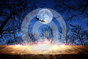 Halloween Holiday concept. Empty rustic table in front of scary and misty night sky, forest and full moon background. Ready for