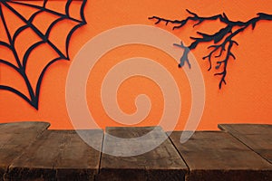 Halloween holiday concept. Empty rustic table in front of Spider webs over orange background. Ready for product display montage.