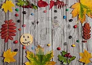 The frame is made of autumn leaves of maple and Rowan, scary smiley on cookies, colorful candies on a wooden background.