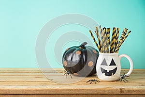 Halloween holiday concept with jack o lantern cup and black pumpkin decor on wooden table