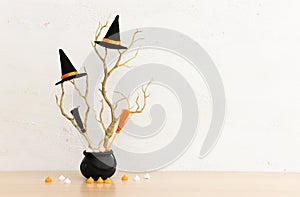 Halloween holoday. witcher cauldron and hat, broom, bare trees, treats over wooden table