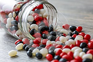 Halloween inspired jar of red, white and black jelly beans spilling out onto a wooden table. A perfect fall sweet treat.