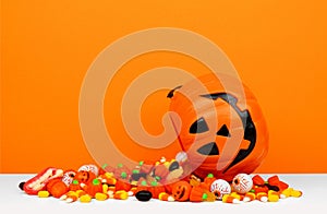 Halloween Jack o Lantern bucket with spilling candy with an orange background