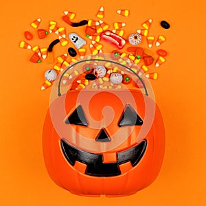 Halloween Jack o Lantern bucket with spilling candy, top view on an orange background