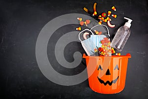 Halloween Jack o Lantern pail with spilling candy and COVID 19 prevention supplies over a black background