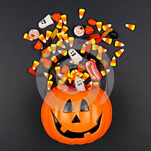 Halloween Jack o Lantern pail with spilling candy, top view on a black background